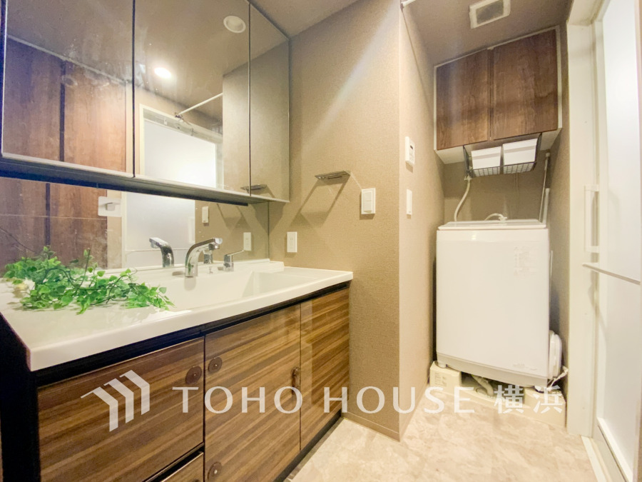 木目調の洗面台と収納が調和した、清潔感あふれる洗面スペース。洗濯機置き場も完備しています。