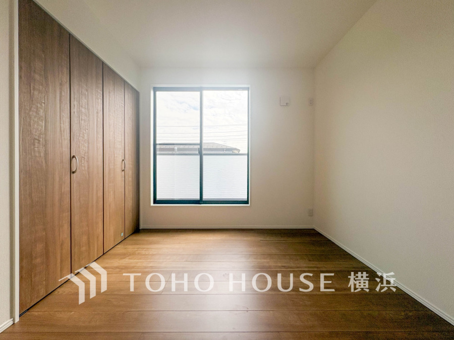 大きな窓から自然光が差し込み、木目調の収納扉が落ち着いた雰囲気を演出するシンプルな洋室です。