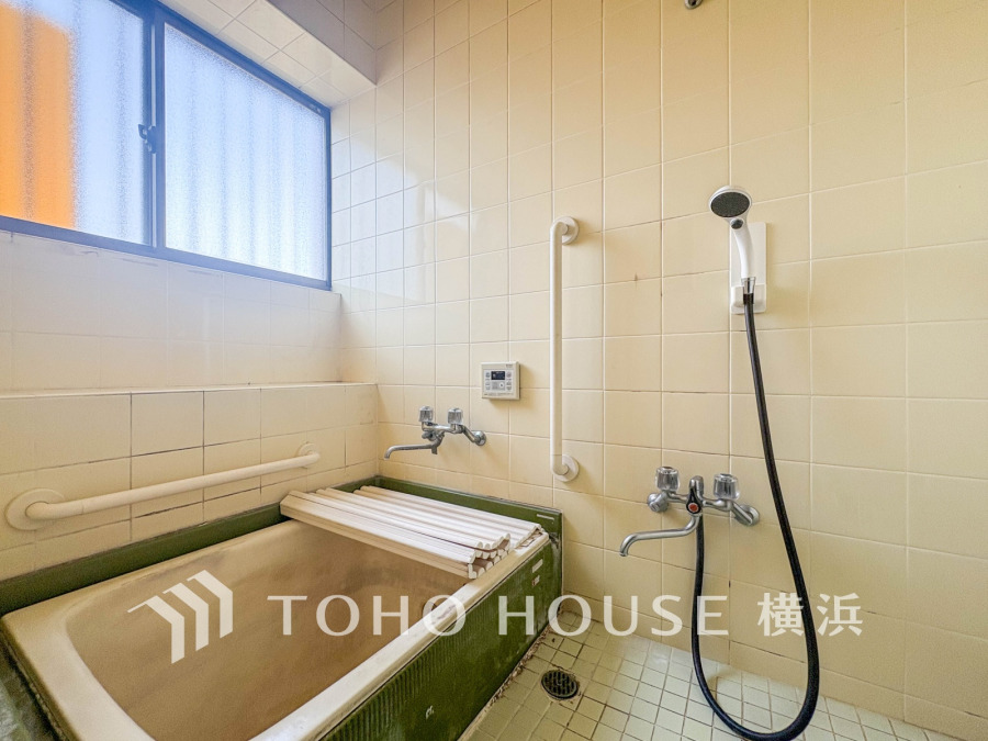 窓から自然光が差し込むレトロなタイル張りの浴室。手すり付きで安全に配慮された空間です。