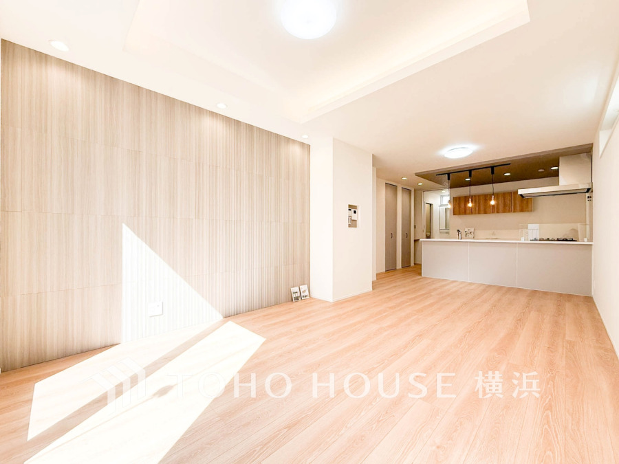 明るい自然光が差し込む広々としたリビング。木目調の壁と床が温かみを演出し、開放的なキッチンと繋がる快適空間です。