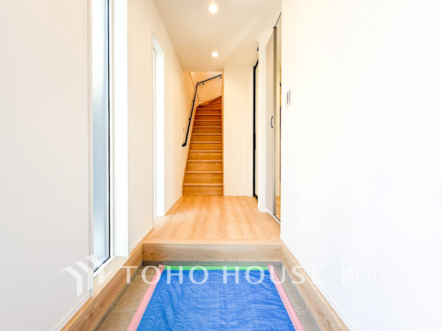 明るく清潔感あふれる玄関ホール。木目調の階段と大きな窓が開放感を演出し、家族を温かく迎えます。