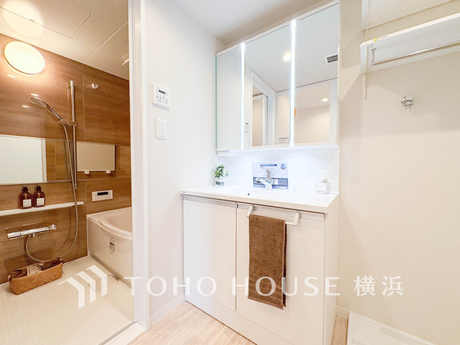 清潔感あふれる洗面台と木目調の浴室が調和した、快適で使いやすいバスルーム空間です。