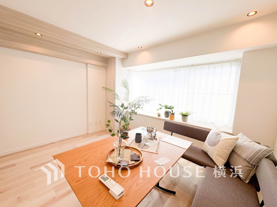 自然光がたっぷり入る明るいリビング。シンプルで温かみのある木製テーブルと落ち着いたソファが寛ぎの空間を演出します。