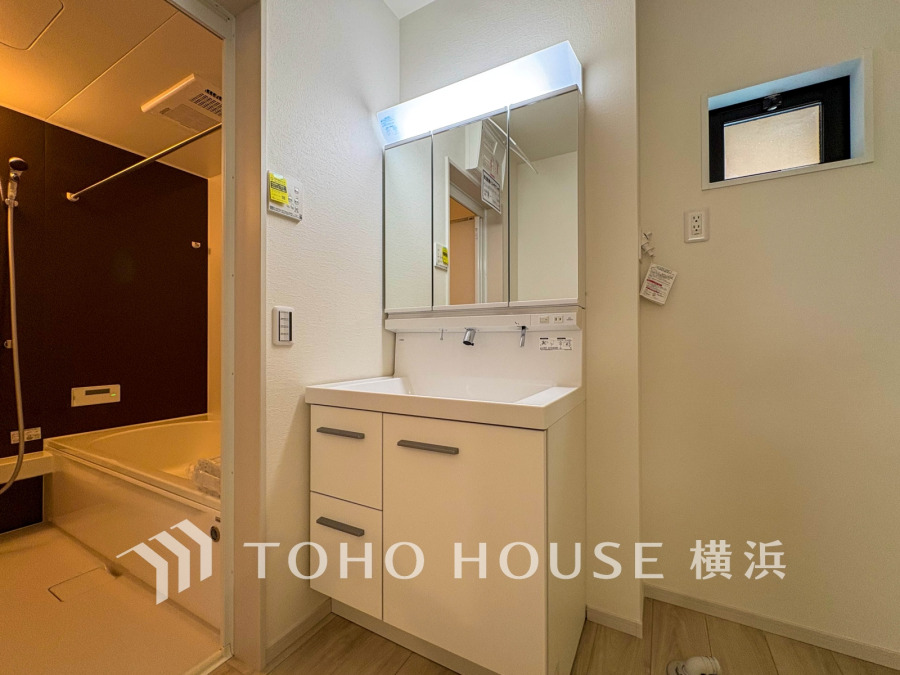 清潔感あふれる洗面台と収納充実の洗面スペース。隣接する浴室は落ち着いたダークカラーで統一されています。