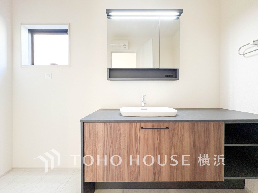 シンプルで清潔感のある洗面台。木目調の収納と広いカウンターで使い勝手も優れています。