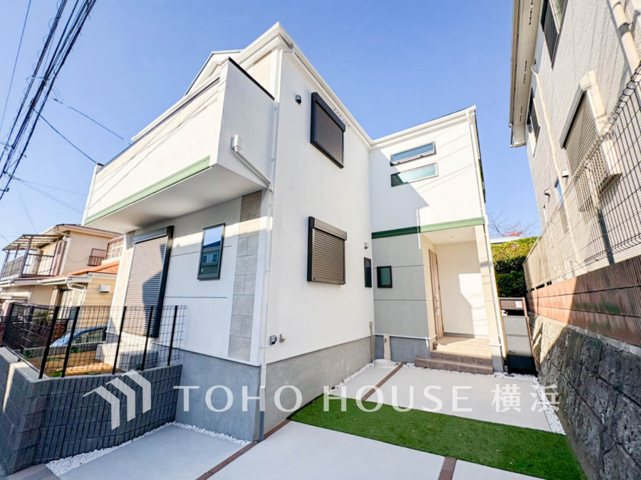 陽当たり良好な新築戸建て。シンプルな白壁と緑のアクセントが調和し、駐車スペースも確保された快適な住まいです。