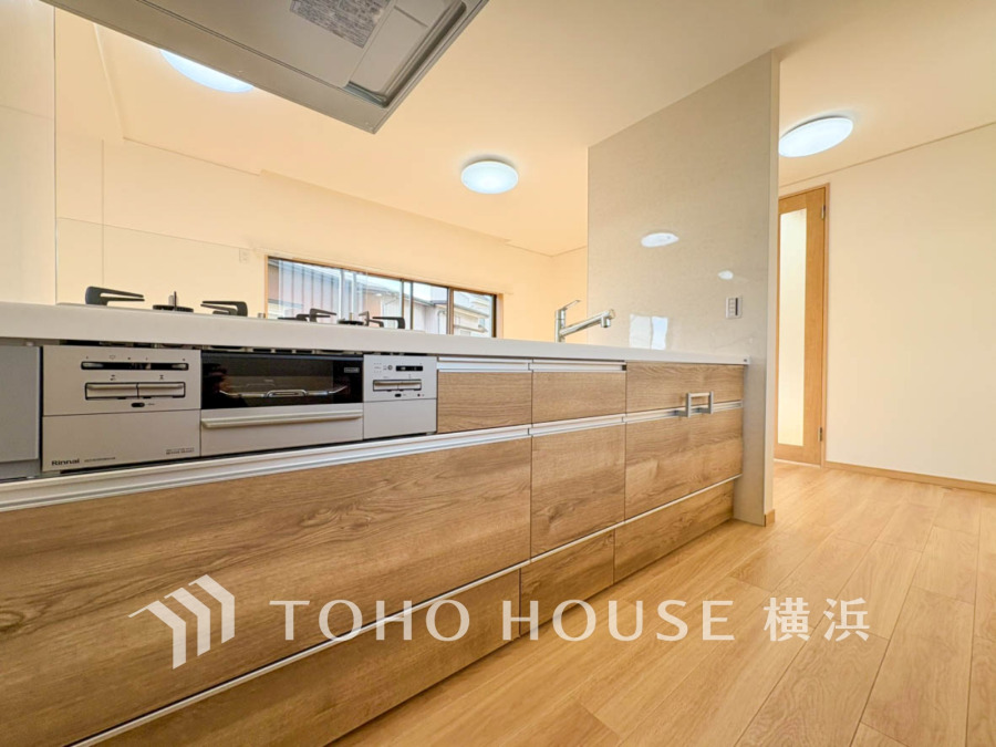 木目調の収納が美しい、開放感あふれる対面式システムキッチン。家族との会話も楽しめる設計です。