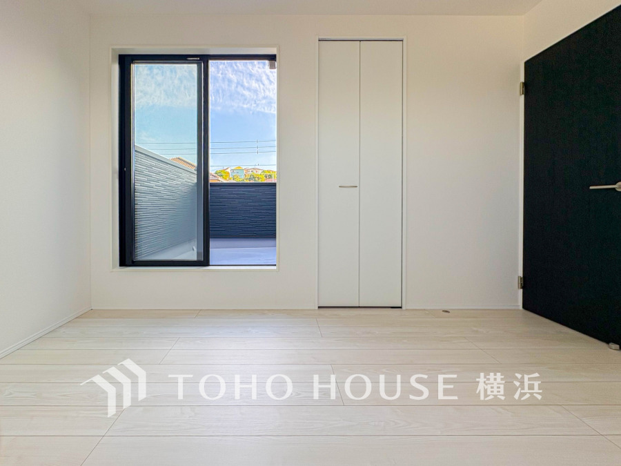 明るい光が差し込むシンプルで清潔感のある洋室。バルコニーに続く窓と収納スペースを備えています。