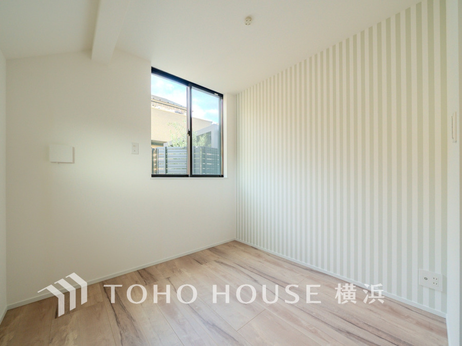 ナチュラルな木目床とストライプ壁紙が調和した、明るく開放的な洋室です。窓からの光で心地よい空間。