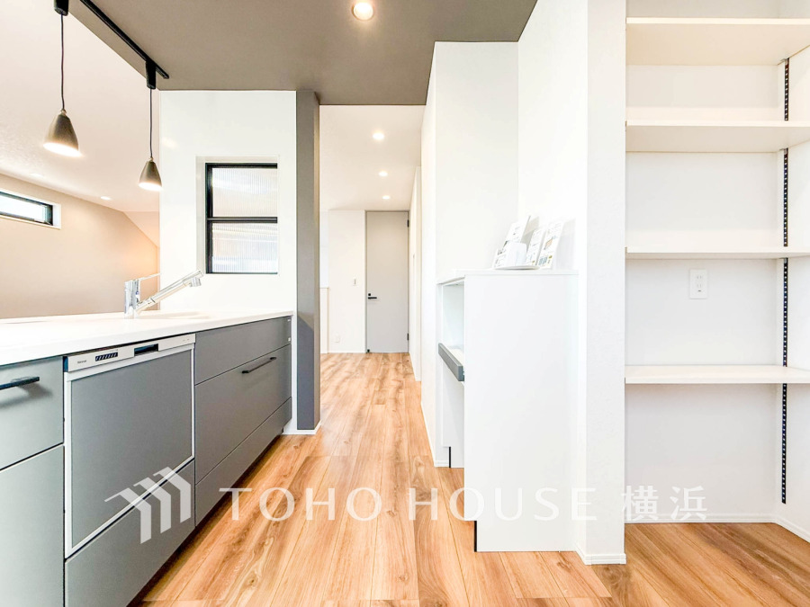 木目フローリングが温かみを演出する、機能的でスタイリッシュなシステムキッチンと収納スペースのある空間です。