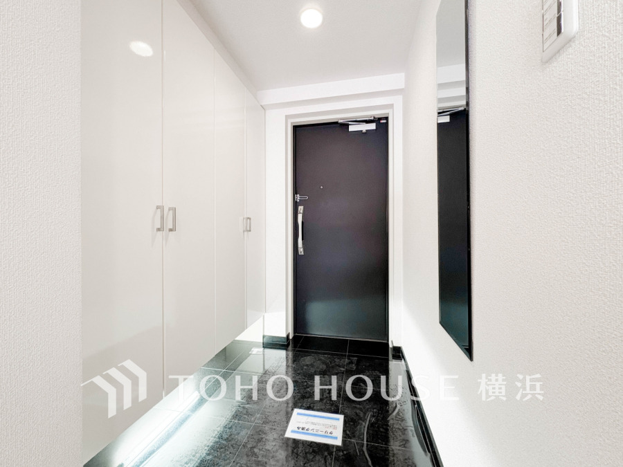 高級感あふれる黒いタイル床とホワイトの収納が調和した、明るく清潔感のある玄関スペースです。