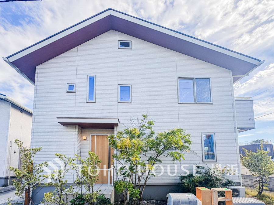 清潔感あふれる白い外壁と木目調の玄関ドアが調和した、明るく開放的な二階建て住宅です。