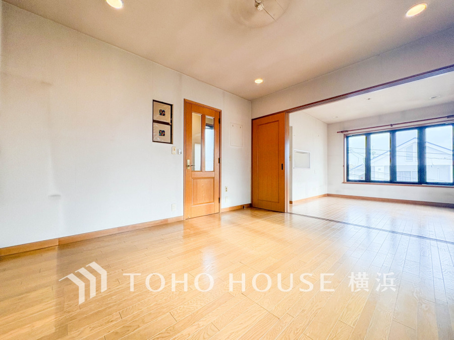 大きな窓から光が差し込む明るい2部屋続きのリビング。木目調の床と扉で温かみのある空間が広がります。