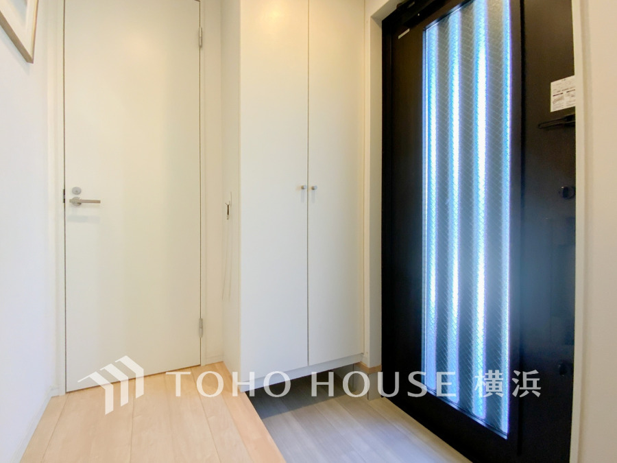 光を取り込む縦長ガラスの玄関扉が印象的な、清潔感あふれるシンプルな玄関スペースです。