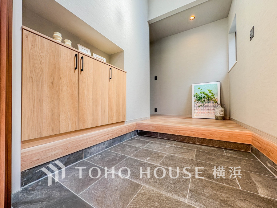 落ち着いた色合いのタイルと木目の収納が調和する、広々とした玄関スペースです。