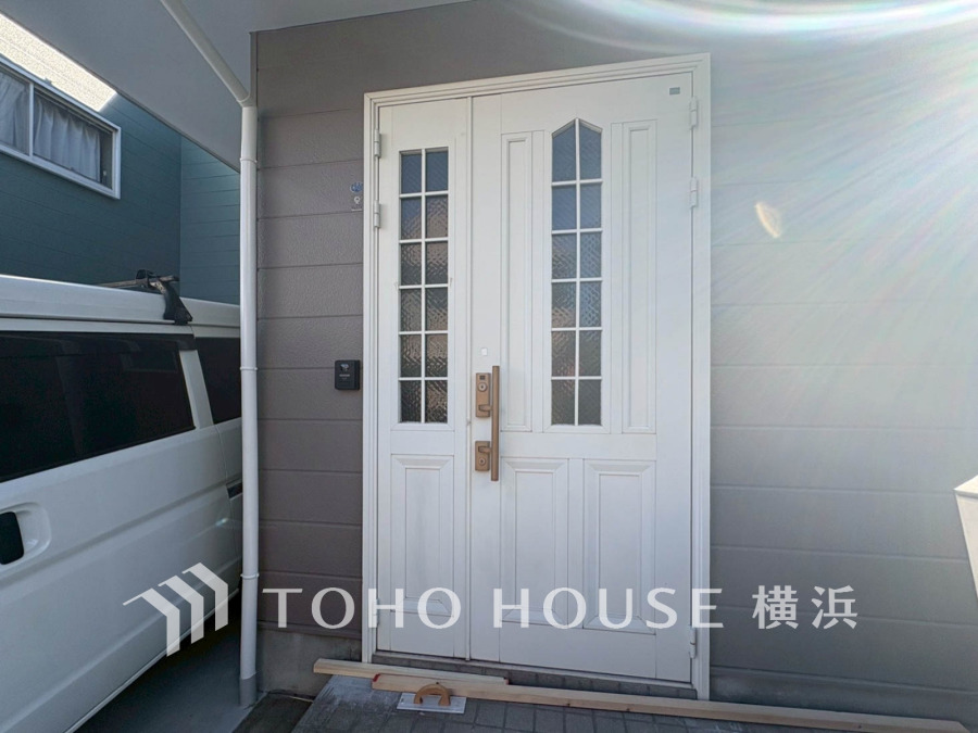 陽射しが差し込む白い玄関扉が、温かみと清潔感を演出する住まいの入口です。