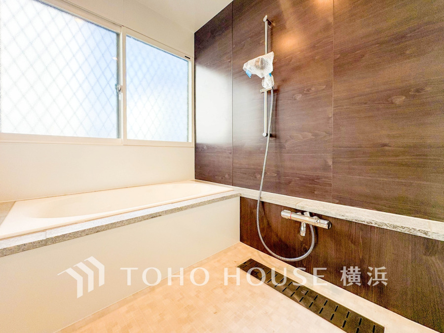 木目調の壁が温かみを演出する、明るく清潔感あふれるバスルーム。大きな窓で換気も快適です。