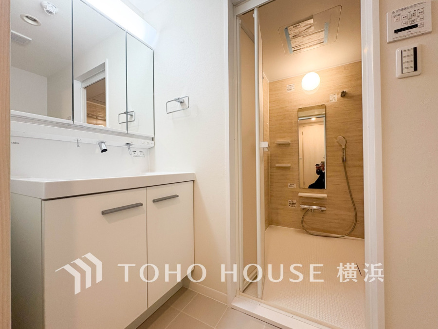 清潔感あふれる洗面台と、木目調パネルが温かみを演出するゆったりとしたバスルームのセットです。