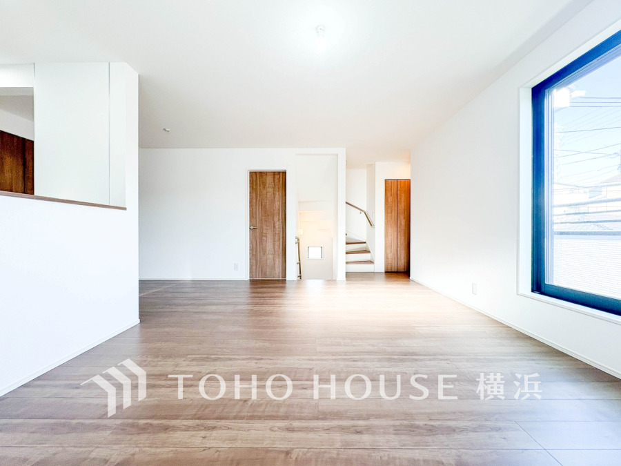 大きな窓から明るい光が差し込む、広々としたリビング。シンプルで温かみのあるフローリングが魅力です。