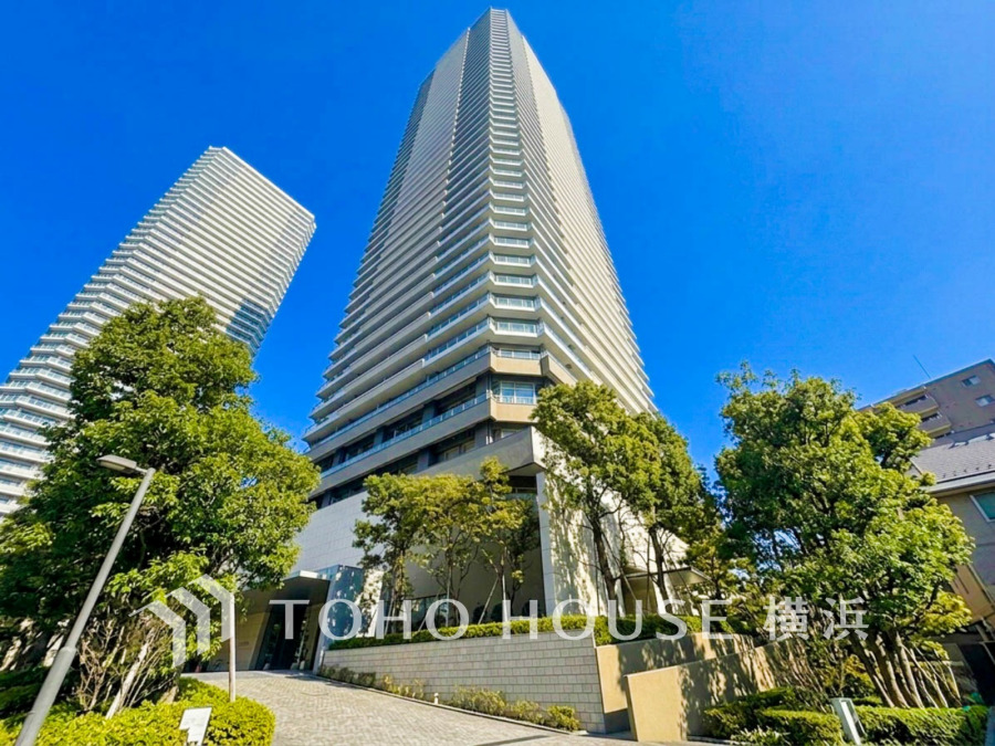青空に映える高層タワーマンション。緑豊かな植栽と共に、都市の快適な暮らしを実現します。