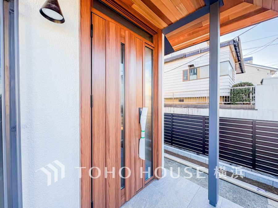 木目調の温かみある玄関ドアと屋根付きポーチが、訪れる人を優しく迎える快適なエントランス空間。