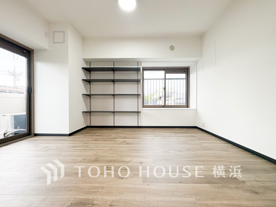 明るい自然光が差し込むシンプルな居室。壁面の収納棚とバルコニーに面した窓が快適な生活空間を演出します。