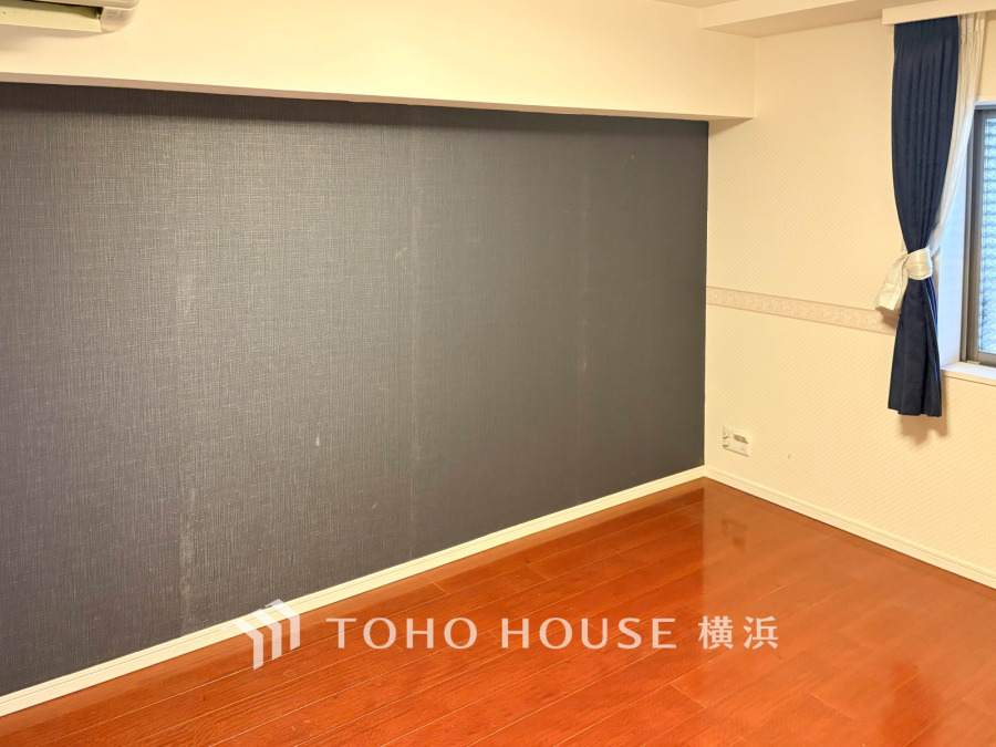 落ち着いたダークカラーのアクセントクロスが印象的な洋室。明るい窓とウッドフローリングが調和した空間です。