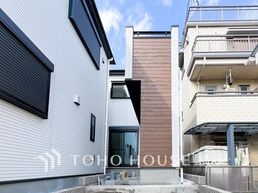 スタイリッシュな木目調外壁が映える、都市型のスリムな新築住宅の外観です。明るい空と調和しています。