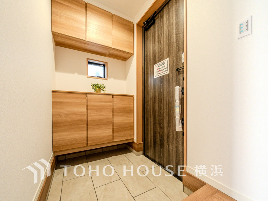 木目調の収納が美しい、明るく清潔感のある玄関スペース。小窓からの自然光で開放感も感じられます。