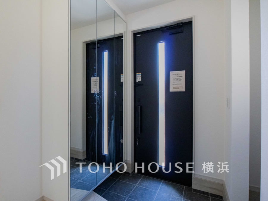 光を取り込む縦長窓付き玄関ドアと、姿見付きの収納で機能的な明るい玄関スペースです。