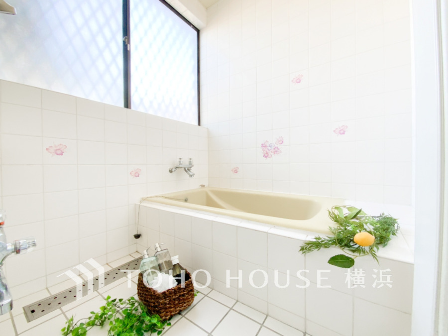 清潔感あふれる白タイルの浴室。明るい窓から自然光が入り、リラックスできる空間を演出しています。