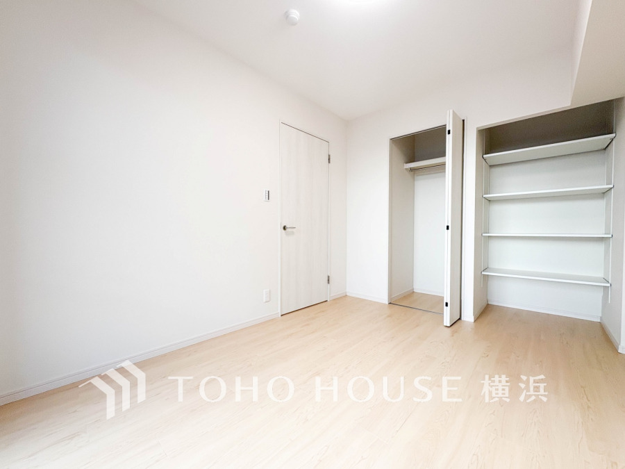 明るい光が差し込むシンプルな洋室。収納スペースと棚が備わり、使い勝手良好です。
