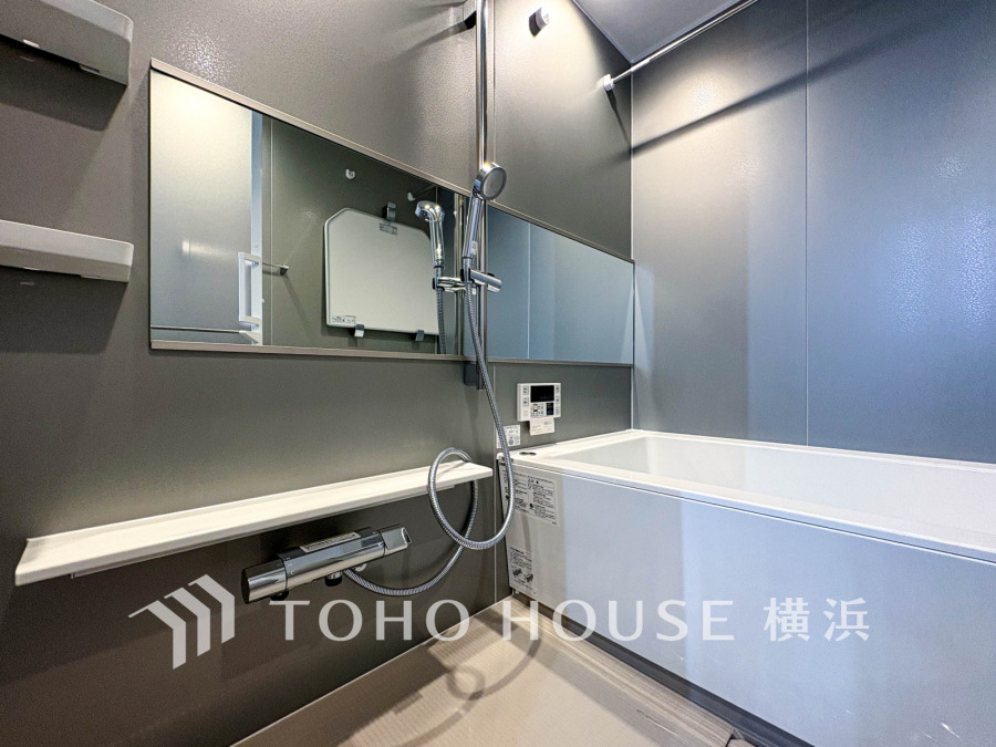 シンプルで清潔感のあるデザインのバスルーム。ワイドミラーとシャワー設備で快適な入浴時間を演出します。