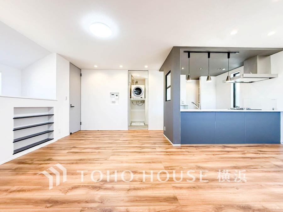 ナチュラルな木目フローリングとダークカラーのキッチンが調和した、明るく開放的なリビング空間です。