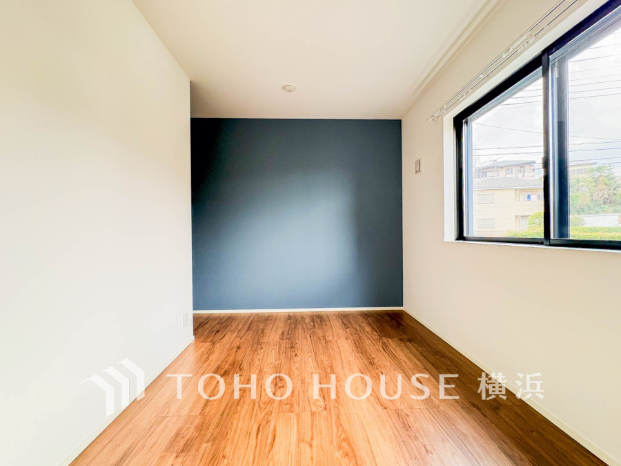 落ち着いたアクセントクロスが映える、明るい自然光が差し込むシンプルな洋室です。