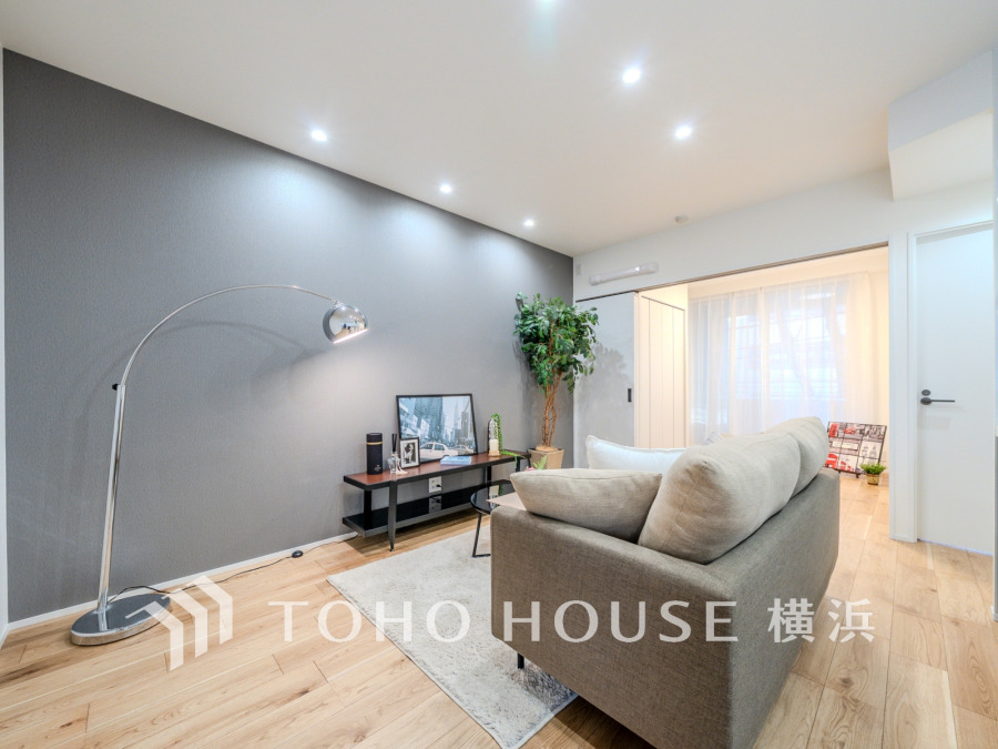 落ち着いたグレーのアクセントウォールと柔らかな照明が調和する、開放感あふれるリビング空間です。