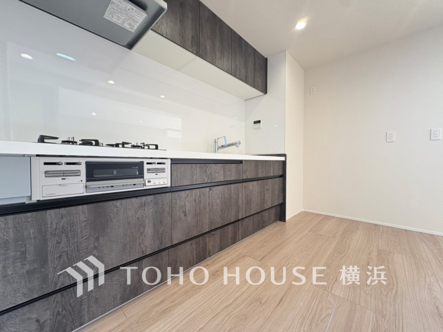 シックな木目調キャビネットと白いワークトップの清潔感あふれるキッチン空間。収納力も充実しています。