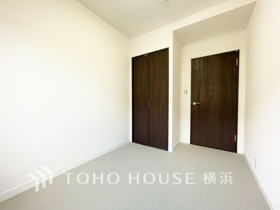シンプルで清潔感のある洋室。ダークブラウンの扉が落ち着いた雰囲気を演出し、収納も充実しています。