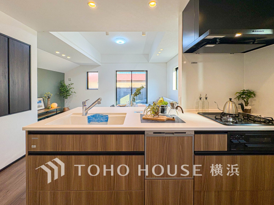 木目調の収納と白いカウンターが調和した対面キッチン。リビングとつながり、開放感あふれる空間です。