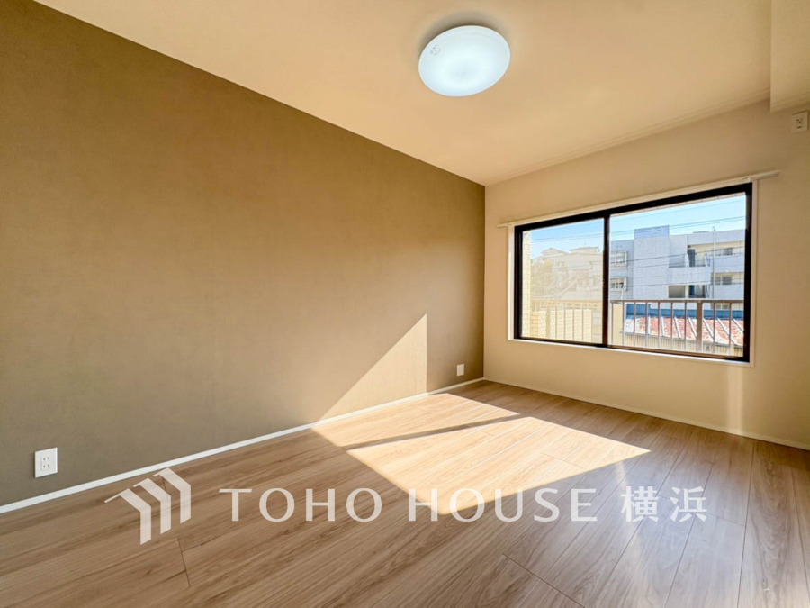 大きな窓から陽光が差し込む、落ち着いたアクセントクロスが魅力の明るい洋室です。