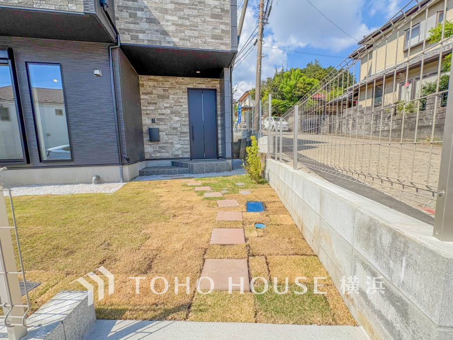 整備された庭と石畳のアプローチが魅力の、モダンな外観の住宅入口です。明るい陽射しが差し込みます。