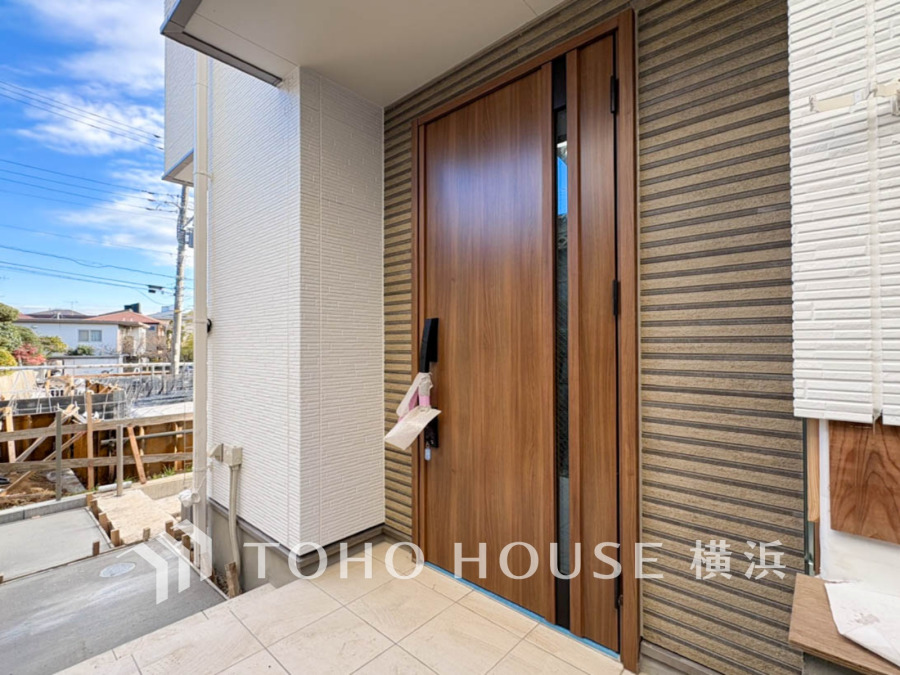 木目調の玄関ドアが暖かみを演出し、広々としたタイル貼りのポーチがゆったりとした迎賓空間を創出します。