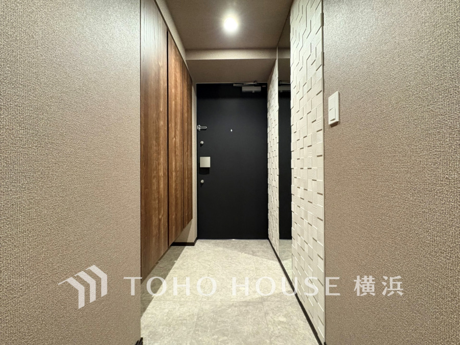 落ち着いた色調の壁と木目調の収納が調和する、ゆったりとした玄関ホール。鏡と間接照明で明るさも確保。