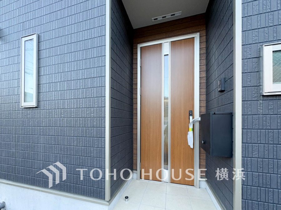 木目調のドアが印象的な玄関。落ち着いたダークグレーの外壁と調和し、スタイリッシュな印象を与えます。