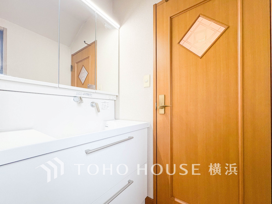 清潔感あふれる白い洗面台と木目調のドアが調和した、明るく使いやすい洗面スペースです。