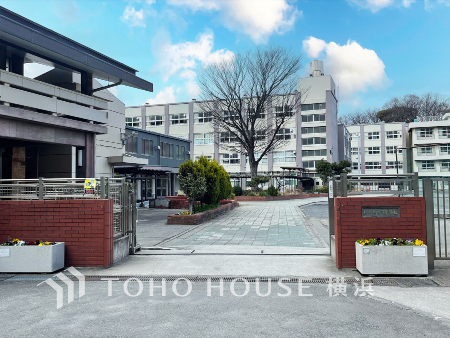 広々とした校庭と緑豊かな植栽が魅力の、閑静な住宅街にある中学校の正門風景です。