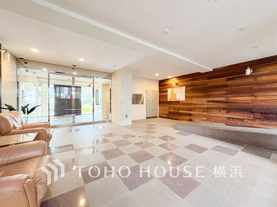 木目調の壁が温かみを演出する、明るく開放的なマンションエントランスホールです。