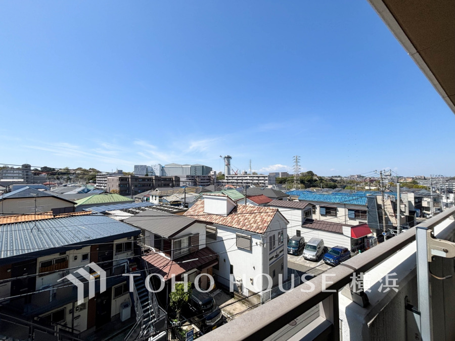 晴天の下、開放感あふれるバルコニーから住宅街と遠くの緑地が広がる眺望を一望できます。