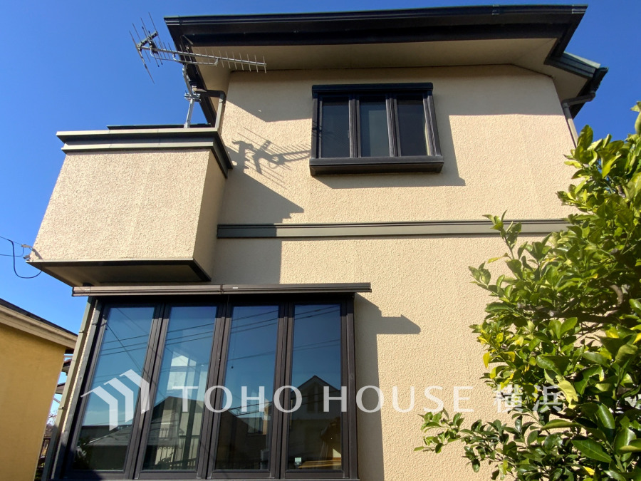 明るい日差しが降り注ぐ、落ち着いた色合いの外壁と大きな窓が魅力の2階建て住宅です。