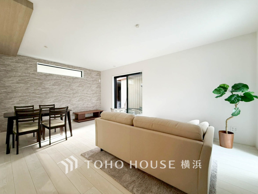 明るい光が差し込むシンプルで落ち着いたリビング。ナチュラルな色合いとグリーンが調和した空間です。